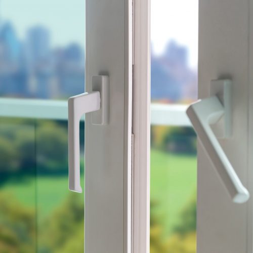 Sliding door of a balcony. Close-up of the lock on the door with and view of the city at background. White PVC door and security glass.